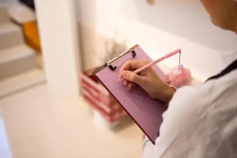 Person writing on pink clipboard with pen