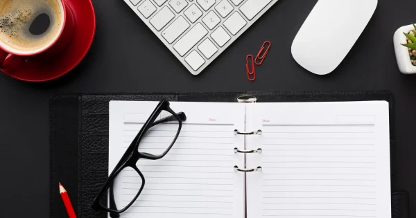 Workspace with coffee, keyboard, glasses, and notebook.