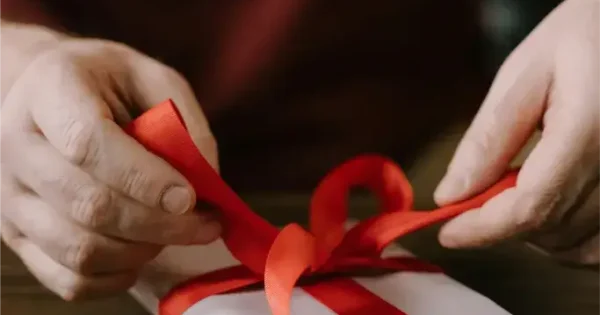 Person tying red ribbon on wrapped gift